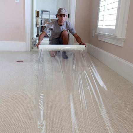 painter rolling out carpet protection film over carpet surface